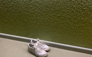 Paar schone witte sneakers op de vloer tegen een olijfgroene muur